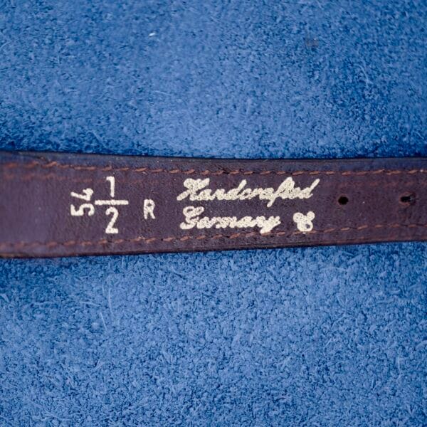A close-up of the Ernest Borel Kaleidoscope Cocktail Brown Dial on a blue fabric background, marked with 5 1/2 R, Germany, and Leidenfeld, printed in white alongside a small decorative symbol.