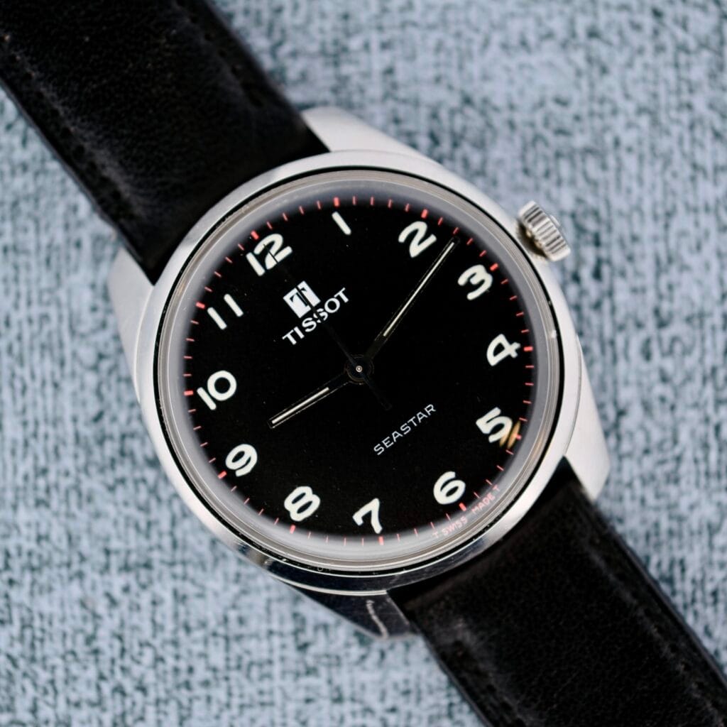 Tissot Seastar Manual Wind Arabic Numerals watch with a black dial and leather strap, displayed on a light textured surface.