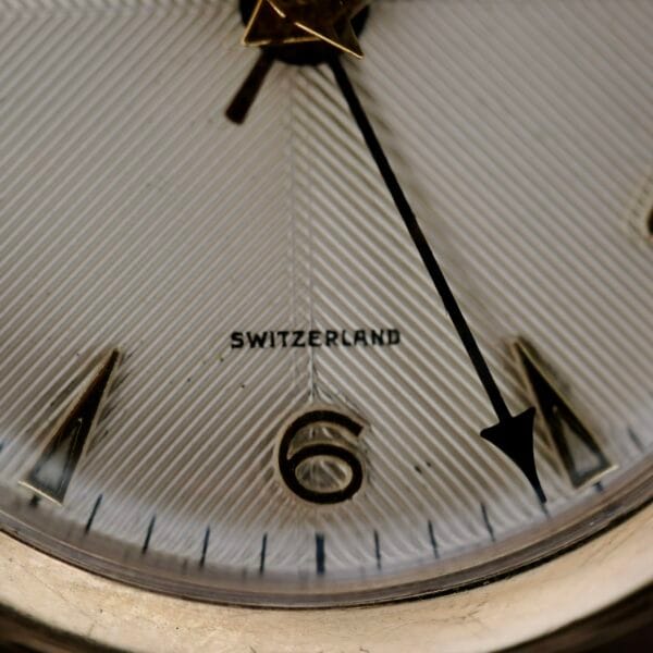 Close-up of a Vulcain Cricket 120 Radial Dial wristwatch, featuring SWITZERLAND above the number 6. The hour hand is slightly past 11, and the minute hand near 12 on its textured dial.