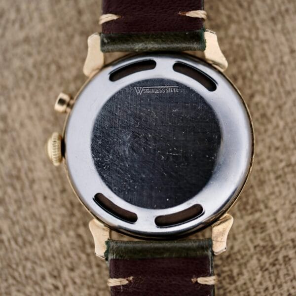 Close-up of the back of a Vulcain Cricket 120 Radial Dial Crab Lugs wristwatch, featuring a round stainless steel case marked STAINLESS STEEL and a brown leather strap with visible stitching. The surface is slightly scratched and worn.