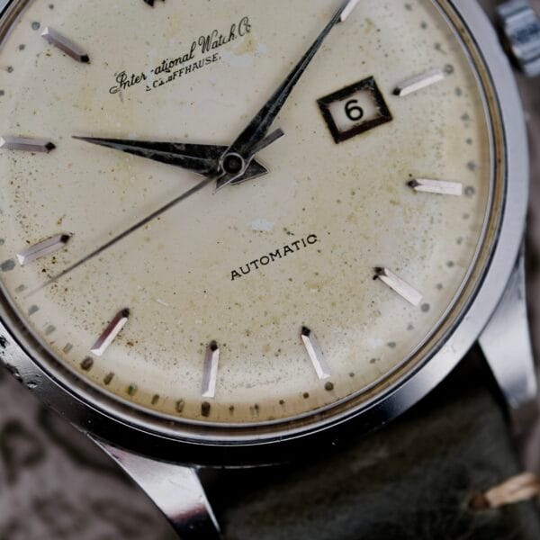 Close-up of an IWC Stainless Steel Automatic C.853 wristwatch with a weathered cream-colored face, black hands, a date window showing 6, and marked with International Watch Co. and Automatic, featuring a leather strap.