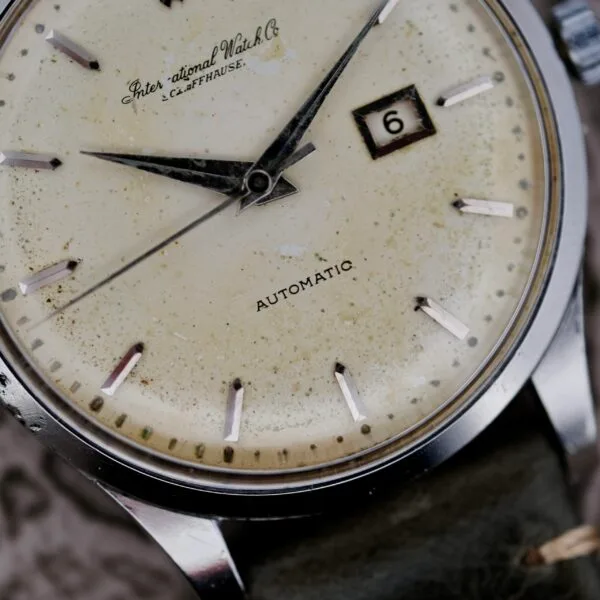 Close-up of an IWC Stainless Steel Automatic C.853 wristwatch with a weathered cream-colored face, black hands, a date window showing 6, and marked with International Watch Co. and Automatic, featuring a leather strap.