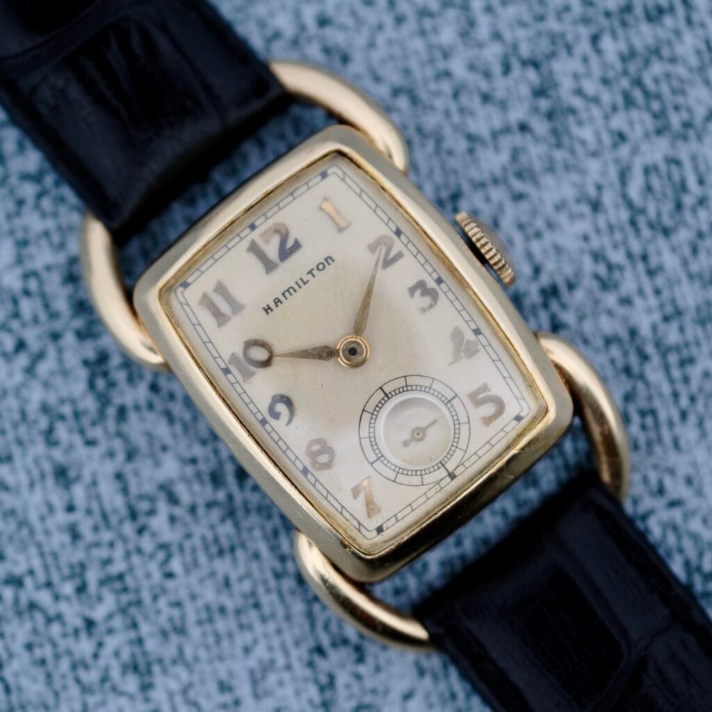 The 1940s Hamilton Bowman wristwatch with a black leather strap rests on a textured gray surface, showcasing classic vintage elegance.