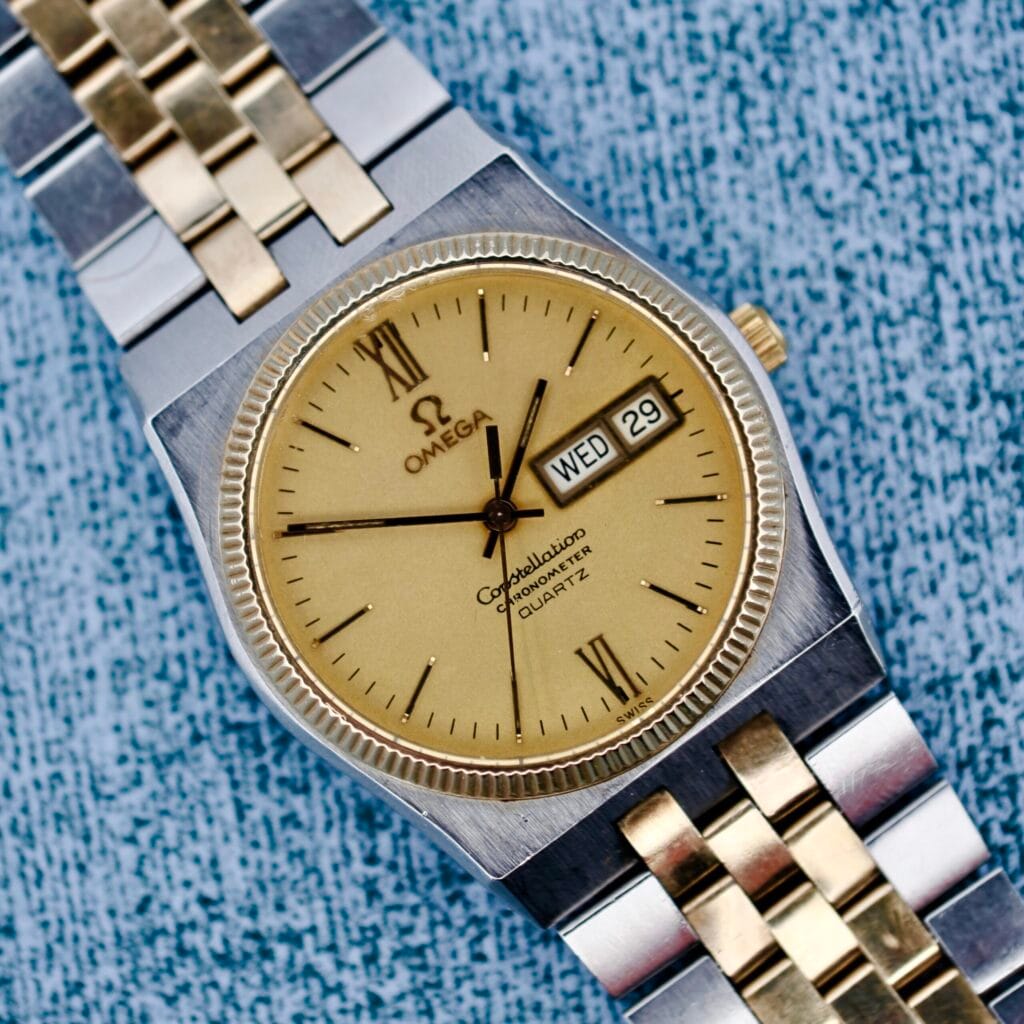 The Omega Constellation Chronometer Quartz features a two-tone case and displays the day and date on a textured blue dial.