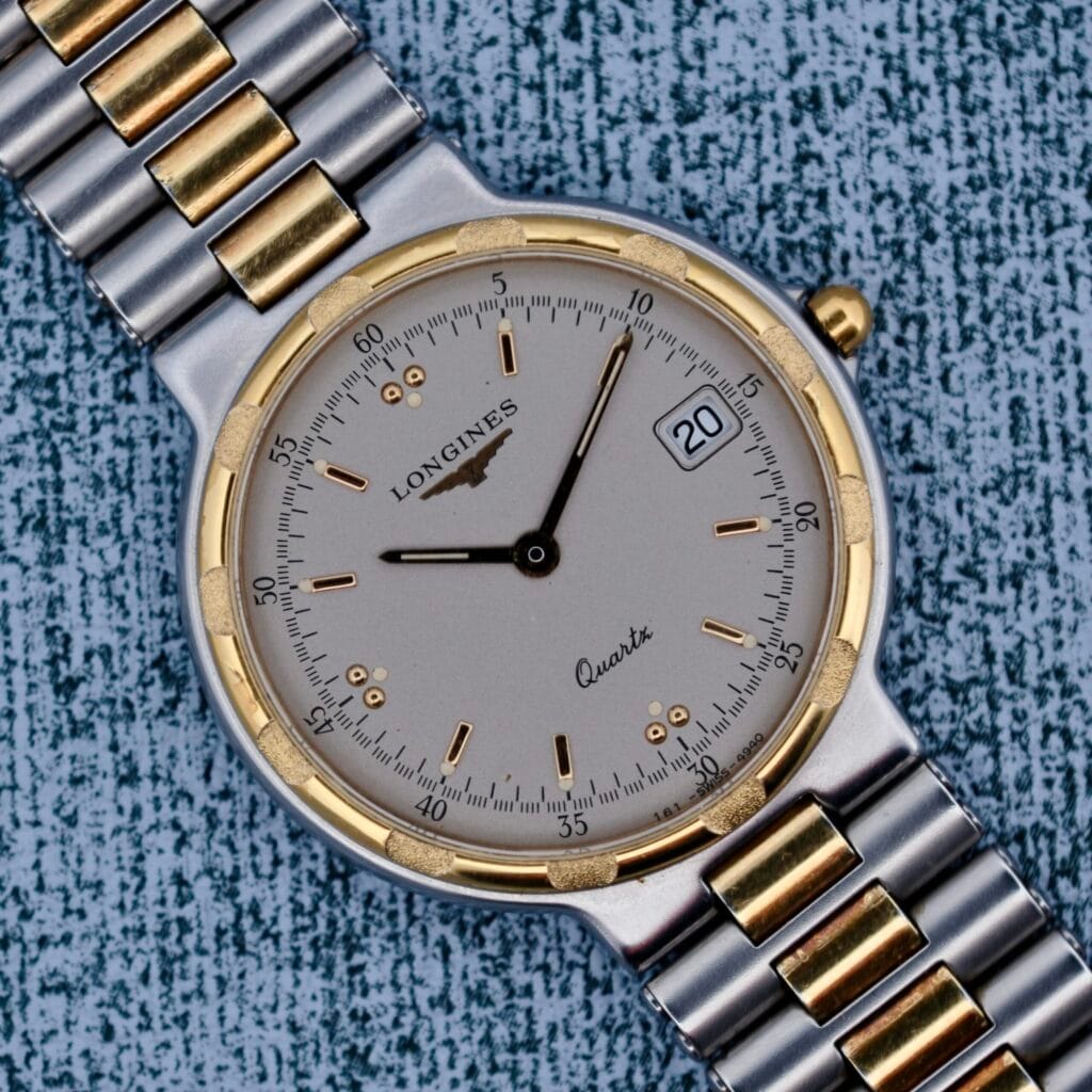 A Longines Conquest Quartz Two-Tone 4940, featuring a silver and gold band, rests on a textured blue surface.