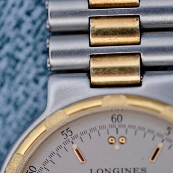 Close-up of the Longines Conquest Quartz Two-Tone 4940, showcasing its watch face and metallic band. It features a two-toned design with gold accents on a silver background, and the brand name is partially visible. The linked band alternates between gold and silver links.