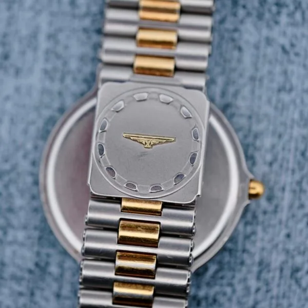 A Longines Conquest Quartz Two-Tone 4940 wristwatch rests on a textured surface, showcasing a brushed steel face with a central gold detail and a two-tone bracelet of alternating silver and gold links.