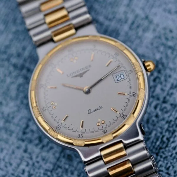 Close-up of the Longines Conquest Quartz Two-Tone 4940. It features a round stainless steel and gold face, a date window on the right, quartz movement labeling, and a linked bracelet with the brand name visible on the dial.