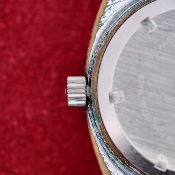 Close-up of the Clinton World Timer Automatic Day/Date wristwatch, highlighting the textured crown and part of its metal case against a red textured background.