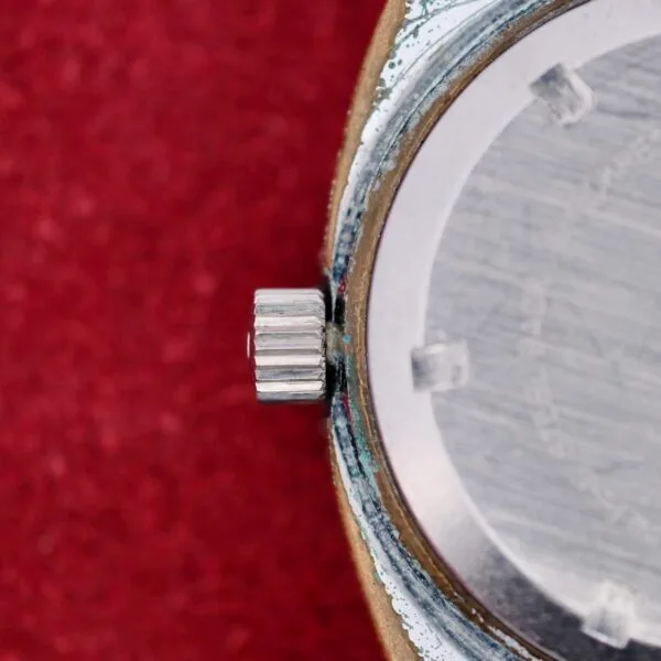 Close-up of the Clinton World Timer Automatic Day/Date wristwatch, highlighting the textured crown and part of its metal case against a red textured background.