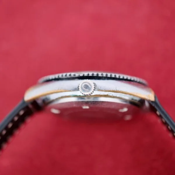 Close-up side view of the Clinton World Timer Automatic Day/Date wristwatch with a black leather strap, silver crown featuring a circular logo, set against a solid red background.