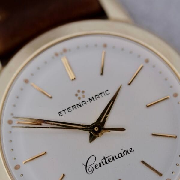 Close-up of a 1950s Eterna Centenaire Eterna Matic Cal. 1428U wristwatch with gold hour markers and hands, brand name on dial, showing 8:22 and paired with a brown leather strap.