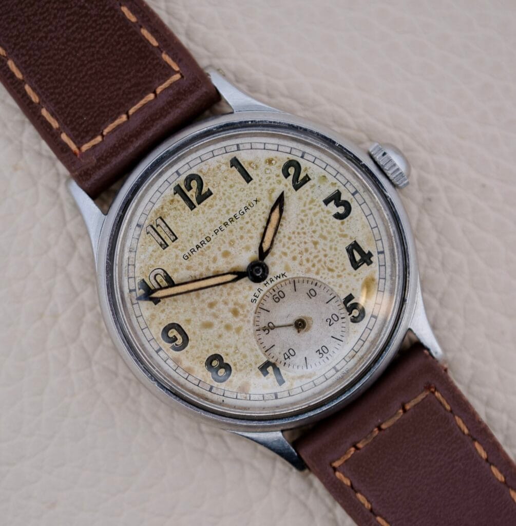 Close-up of a Girard Perregaux Sea Hawk Military Circa 1943 wristwatch featuring a brown leather strap and a speckled vintage dial, evoking classic military style.