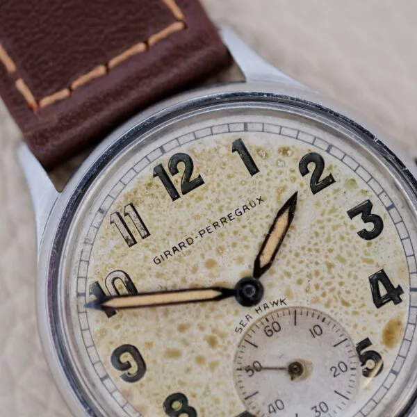 A vintage Girard-Perregaux Sea Hawk Military Circa 1943 wristwatch featuring a brown leather strap, aged cream dial with black numerals, and two hands set to 11:41. The dial displays patina and wear.