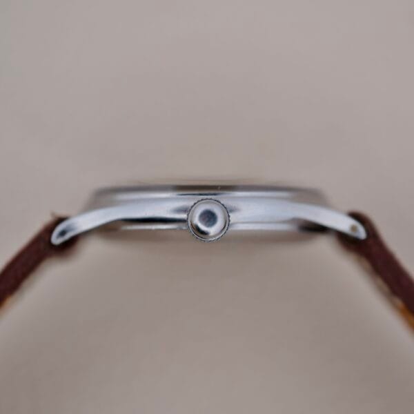 A close-up side view of the Girard Perregaux Sea Hawk Military Circa 1943 wristwatch shows a silver metal case with a central crown and brown leather straps, set against a plain, light background.