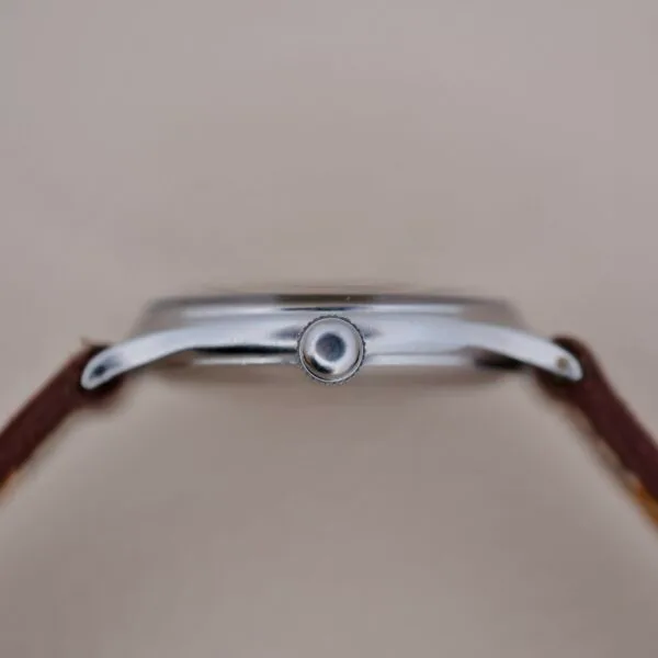 A close-up side view of the Girard Perregaux Sea Hawk Military Circa 1943 wristwatch shows a silver metal case with a central crown and brown leather straps, set against a plain, light background.