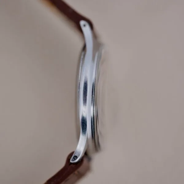 Side view of the Girard Perregaux Sea Hawk Military Circa 1943 with a silver metal case and brown leather strap, shot against a plain light background. The focus is on the profile of the watch’s case.