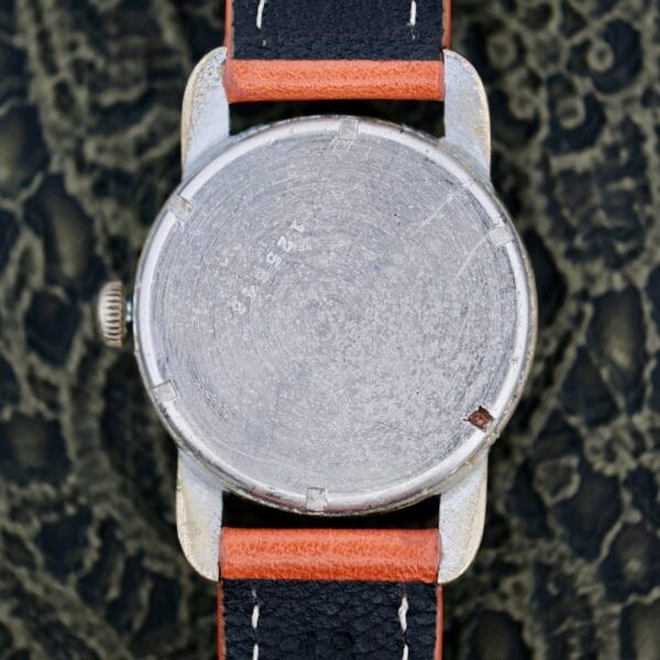A close-up of the back of a 1940s Fairfax Military Incabloc Manual Wind watch with minor scratches and engraved numbers, featuring a two-tone brown and black leather strap, resting on a textured dark surface.