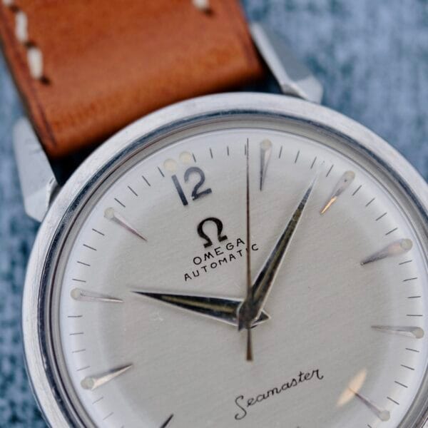 Close-up of an Omega Seamaster Automatic 2832-15 wristwatch with a brown leather strap, silver case, and silver dial showing approximately 10:10. The Omega logo and text are clearly visible.