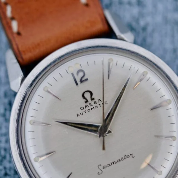 Close-up of an Omega Seamaster Automatic 2832-15 wristwatch with a brown leather strap, silver case, and silver dial showing approximately 10:10. The Omega logo and text are clearly visible.