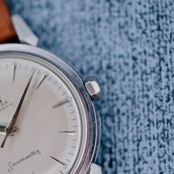 A close-up of the Omega Seamaster Automatic 2832-15 with a silver case, beige dial, and brown leather strap, resting on a textured blue-grey surface.