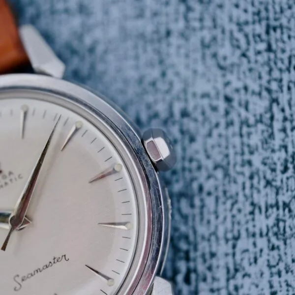 A close-up of the Omega Seamaster Automatic 2832-15 with a silver case, beige dial, and brown leather strap, resting on a textured blue-grey surface.