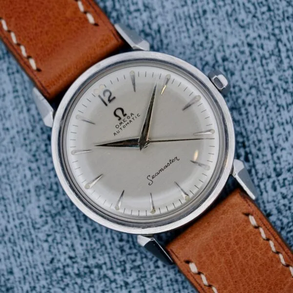 A close-up of the Omega Seamaster Automatic 2832-15 wristwatch, featuring a silver dial, black hour markers, silver hands, and a brown leather strap, displayed on a textured gray surface.