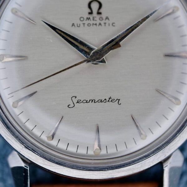 Close-up of the Omega Seamaster Automatic 2832-15 watch face, featuring silver hour markers and hands, with black text on a silver dial. The Omega logo and Seamaster are prominently displayed.