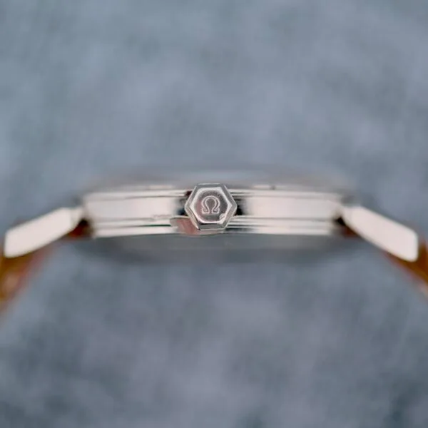 Close-up side view of the Omega Seamaster Automatic 2832-15, a silver wristwatch with a hexagonal crown featuring an engraved logo, set against a blurred gray background.