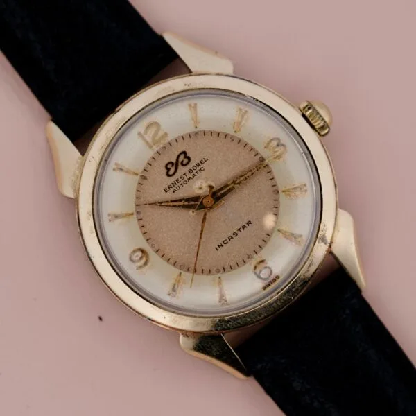 A close-up of the Ernest Borel Incastar 1560 Gold Capped wristwatch, featuring a gold case, black leather strap, Arabic numerals, and gold hour, minute, and second hands. The dial displays Ernest Borel, Automatic, and Incastar.