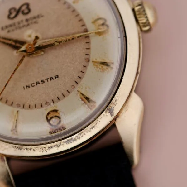 Close-up of an Ernest Borel Incastar 1560 Gold Capped wristwatch with a worn, discolored dial. INCASTAR and SWISS are printed on the face, and the hour hand points near 11.