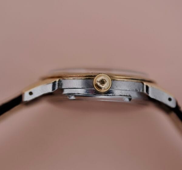 Close-up side view of the Ernest Borel Incastar 1560 Gold Capped wristwatch, highlighting the crown and part of the case with a silver and gold-toned metal finish, set against a plain beige background.