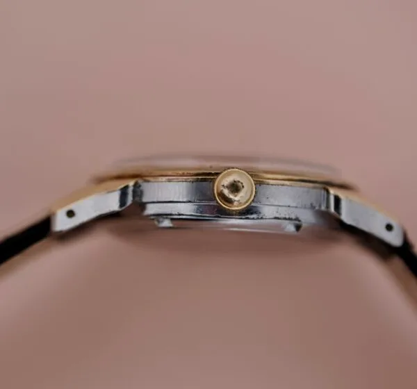 Close-up side view of the Ernest Borel Incastar 1560 Gold Capped wristwatch, highlighting the crown and part of the case with a silver and gold-toned metal finish, set against a plain beige background.