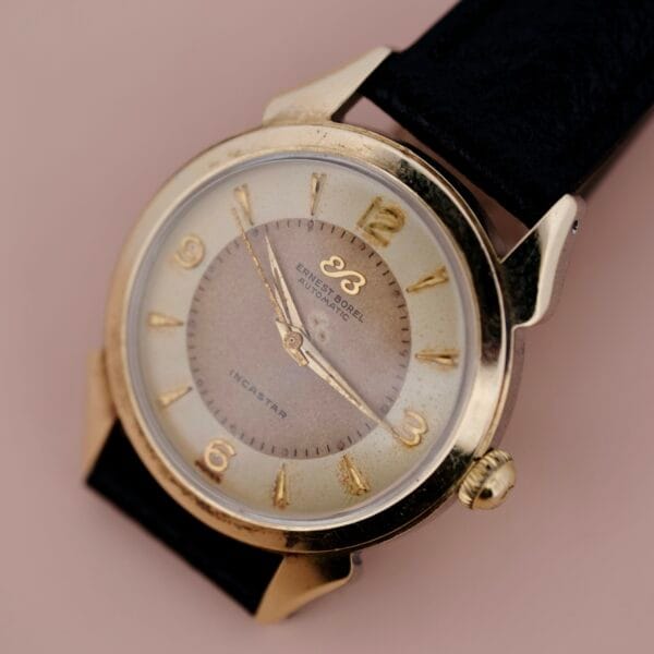 A close-up of the Ernest Borel Incastar 1560 Gold Capped wristwatch, featuring a gold case, gold hour markers, black leather strap, and displaying 2:07 against a neutral background.