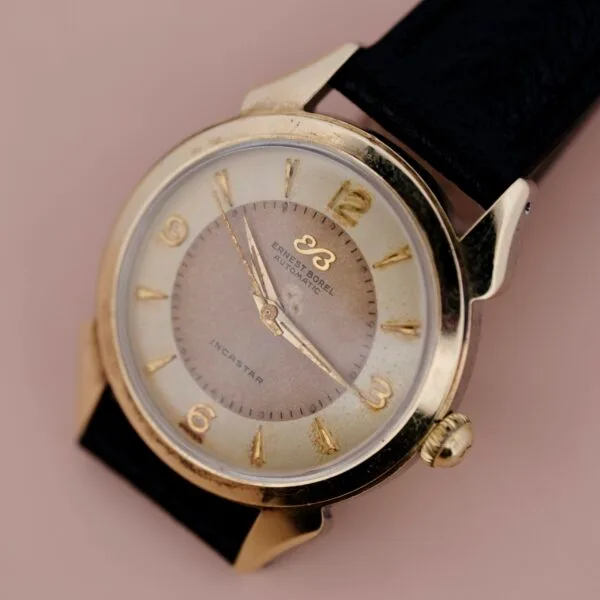 A close-up of the Ernest Borel Incastar 1560 Gold Capped wristwatch, featuring a gold case, gold hour markers, black leather strap, and displaying 2:07 against a neutral background.