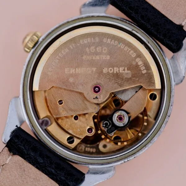 Close-up of the inner mechanical movement of the Ernest Borel Incastar 1560 Gold Capped wristwatch, showing visible gears, metal parts, and engraved text on the golden rotor. The watch features a black and beige leather strap.