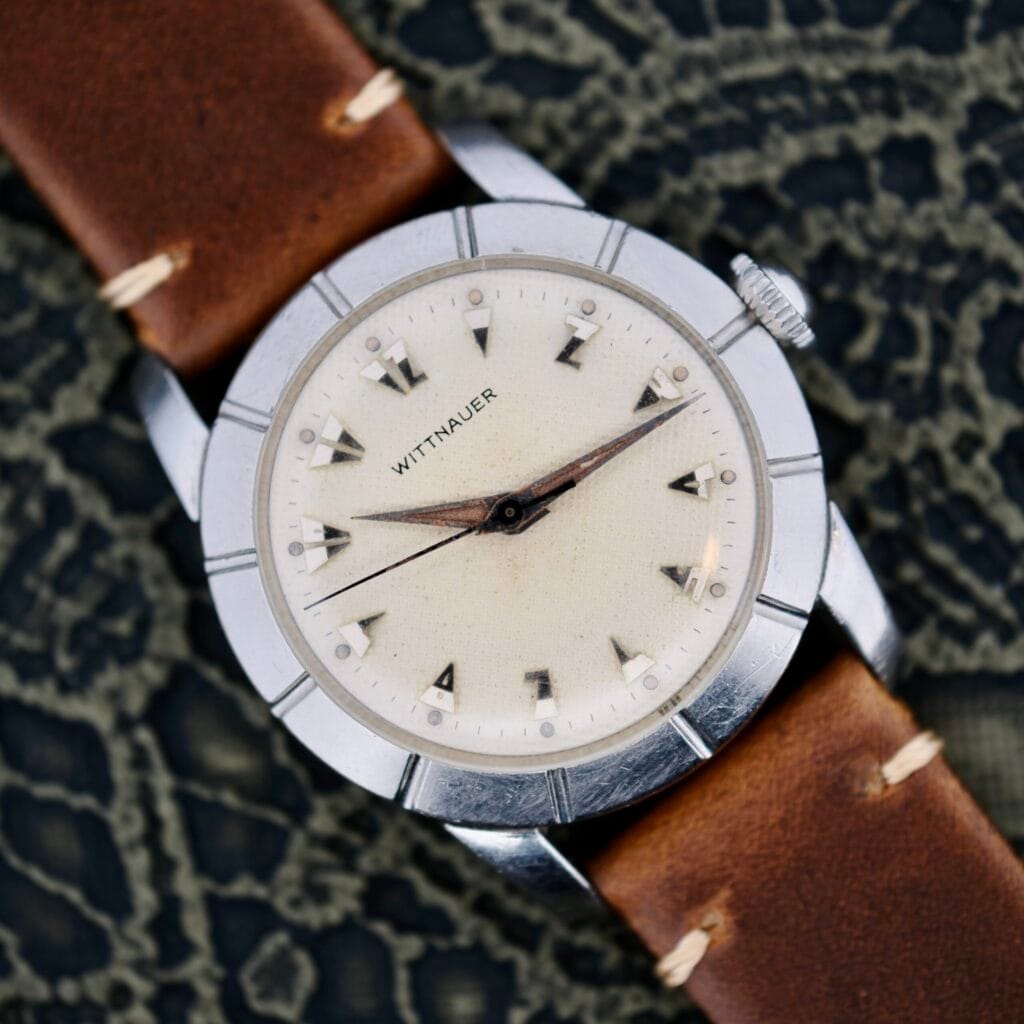 The Wittnauer 2065 Waffle Dial Art Deco Indicies wristwatch features a brown leather strap and is shown against a patterned dark background.
