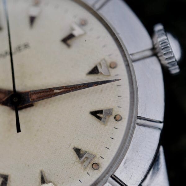 A close-up of the Wittnauer 2065 Waffle Dial shows worn hands, Art Deco indices, and a textured off-white dial. The metallic case and crown display signs of age, highlighting its vintage character.
