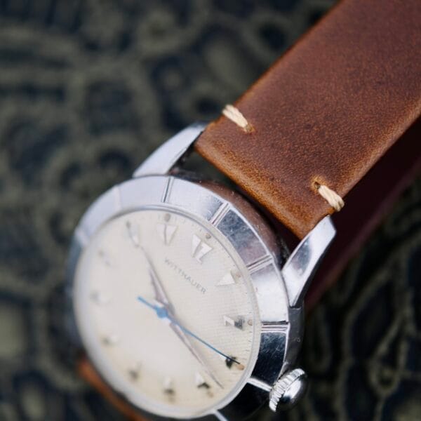 A close-up of the Wittnauer 2065 Waffle Dial wristwatch with Art Deco indices, a cream waffle dial, silver markers, and a brown leather strap, displayed on a textured dark surface.
