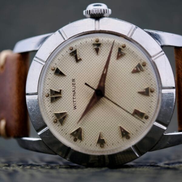 A close-up of the Wittnauer 2065 Waffle Dial with Art Deco indices, featuring a textured beige dial, silver case, triangular hour markers, brown leather strap, and hands at 8:00 and 3:30.