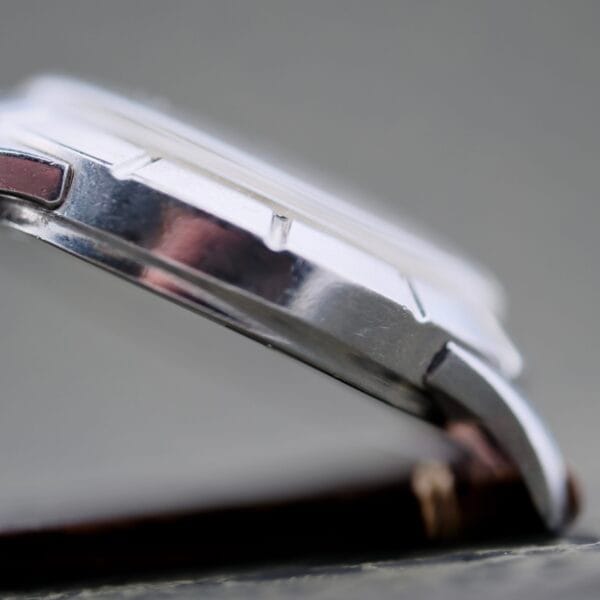 Close-up side view of the Wittnauer 2065 Waffle Dial Art Deco Indices, featuring a silver case with a smooth bezel and brown leather strap, highlighting the watch’s thickness and case edge against a neutral background.