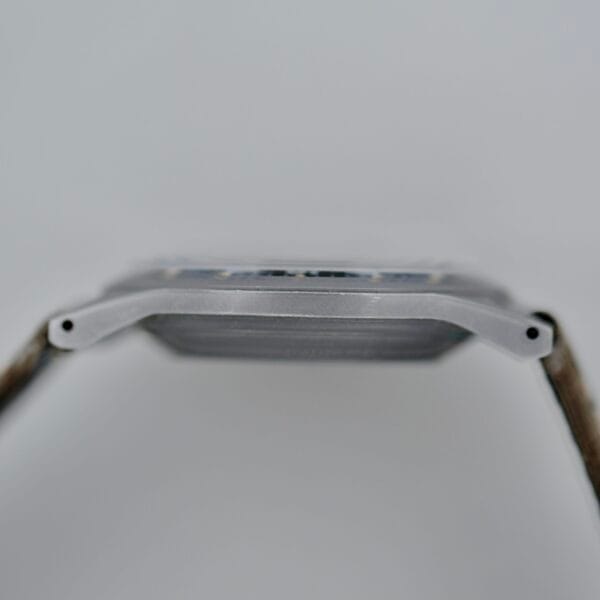 Close-up side view of the 1974 Benrus GG-W-113 U.S. Military Issued wristwatch, showcasing its rectangular metal case, visible lugs, and straps on both sides with a blurred background.