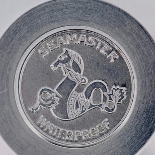 Close-up of the metal emblem on a 1968 Omega Seamaster Deville 165.020, featuring a stylized seahorse with SEAMASTER and WATERPROOF engraved above and below within circular borders.
