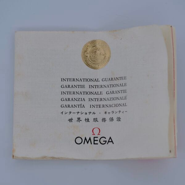 An open booklet for the 1968 Omega Seamaster Deville 165.020 displays the OMEGA logo at the bottom, International Guarantee in various languages above, and a gold seal near the top center of the page.