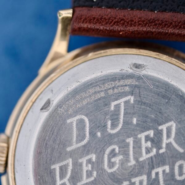 Close-up of the back of a 1950s Wittnauer Automatic Teardrop Lugs watch showing 10K GOLD FILLED BEZEL, STAINLESS BACK, and the engraved name D.T. REGIER above a visible section of the strap.
