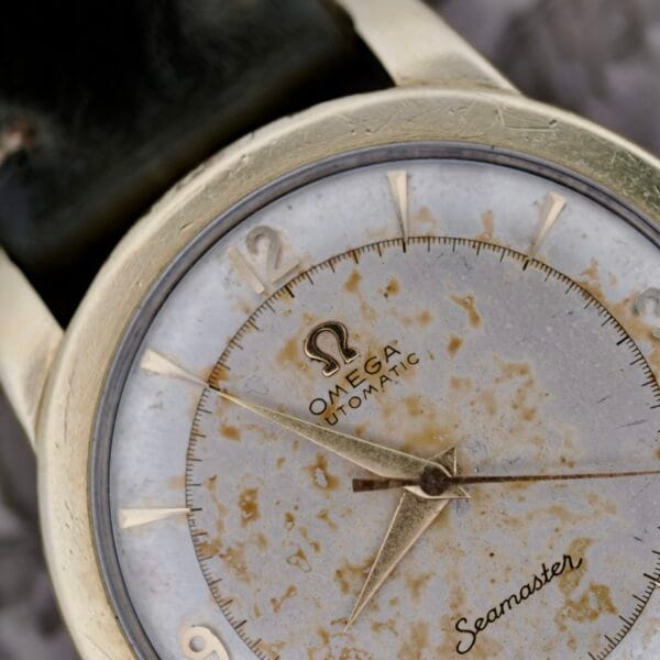 Close-up of an Omega Seamaster Automatic 2577-17 with a tropic dial featuring tarnish and stains, gold-colored case, black leather strap, and visible hour, minute, and second hands.