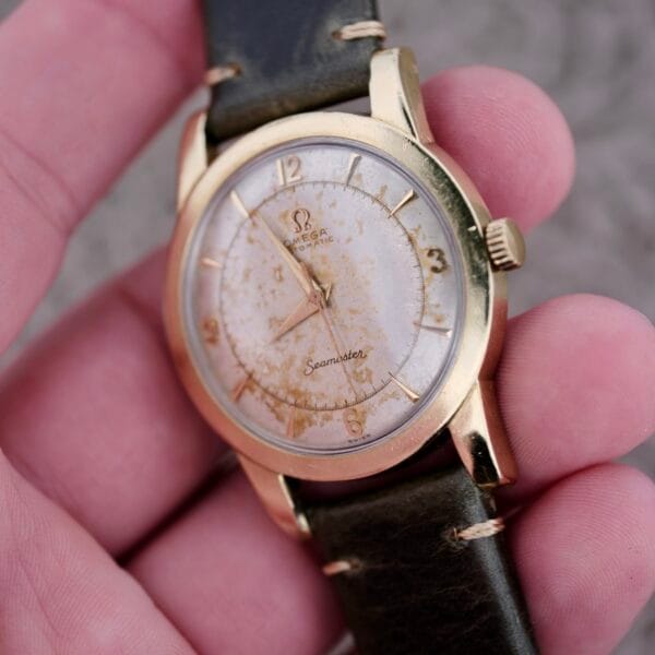 A hand holds an Omega Seamaster Automatic 2577-17 Tropic Dial with a gold case, aged dial, gold hour markers, and a dark leather strap.