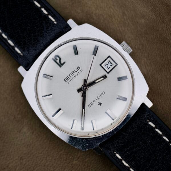A close-up of a silver Benrus Automatic Sea Lord Date wristwatch with a black leather strap, silver dial, black hour markers, date display at 3 oclock, and black hour, minute, and second hands.