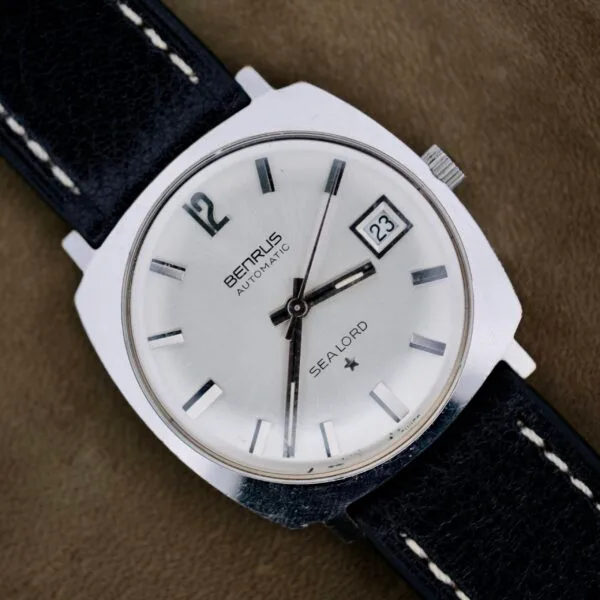 A close-up of a silver Benrus Automatic Sea Lord Date wristwatch with a black leather strap, silver dial, black hour markers, date display at 3 oclock, and black hour, minute, and second hands.