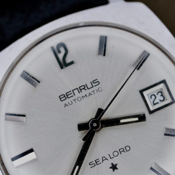 Close-up of a Benrus Automatic Sea Lord Date wristwatch, featuring black and silver hour markers, three hands showing 12:16:36, and the date set to 23.
